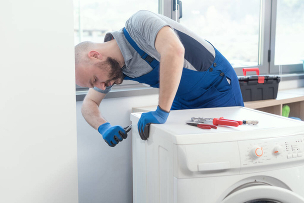 Professional repairman fixing a broken washing machine, home repair concept - Фото, зображення