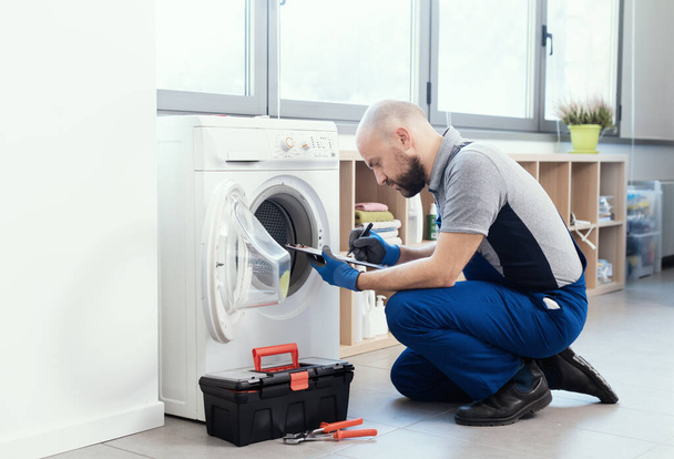 Professional technician writing an invoice after repairing a washing machine, home repair concept - Photo, Image