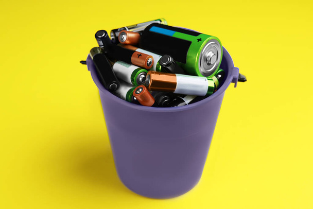 Used batteries in bucket on yellow background, closeup - Zdjęcie, obraz