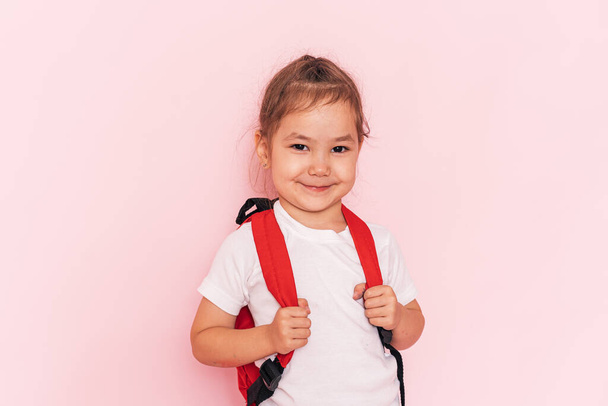 A little girl with a red briefcase stands in front of a pink background. - Foto, Bild