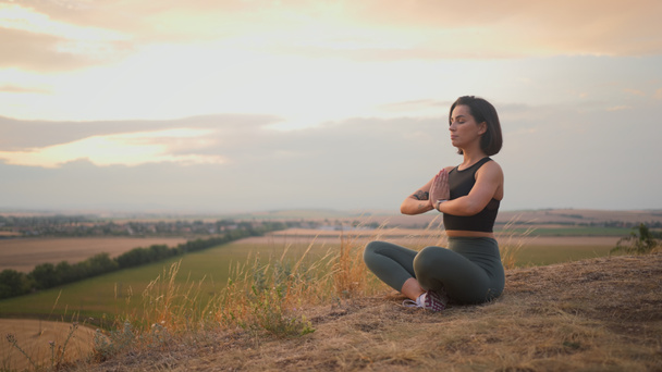 Спокойная спокойная спортивная молодая женщина медитирует, сидя в позе намасте с закрытыми глазами. Девушка делает упражнения дыхания во время отдыха на открытом воздухе - Фото, изображение