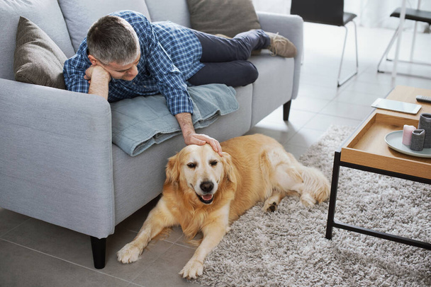 Man relaxing at home and cuddling his dog in the living room - Valokuva, kuva