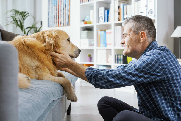 Pet owner spending time with his dog at home in the living room - Fotó, kép