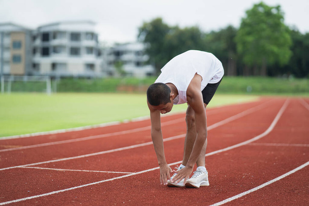 Athletes sport man runner wearing white sportswear to stretching and warm up before practicing on a running track at a stadium. Runner sport concept. - Foto, imagen