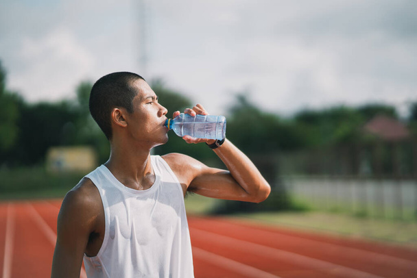 спортсмен держит бутылку воды бегун устал и пить после прохождения тренировки питьевой воды. Концепция спортсмена. - Фото, изображение