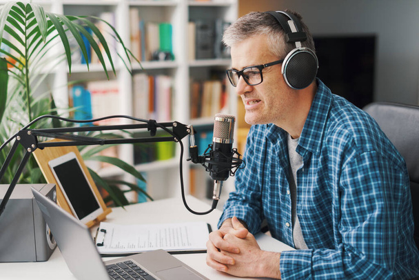 Smiling man wearing headphones and recording audio podcast using a professional microphone - Foto, afbeelding