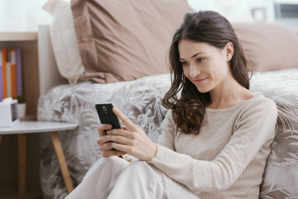 Young woman relaxing on the bed, she watching videos on her smartphone - Foto, Imagen