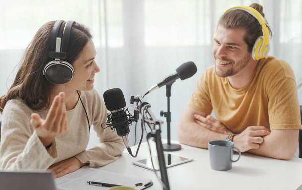 Young man and woman wearing headphones and doing a live podcast for their channel, communication and technology concept - Photo, Image