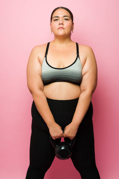 Спортивная женщина с ожирением выглядит решительной во время тренировки с гири во время тренировки - Фото, изображение