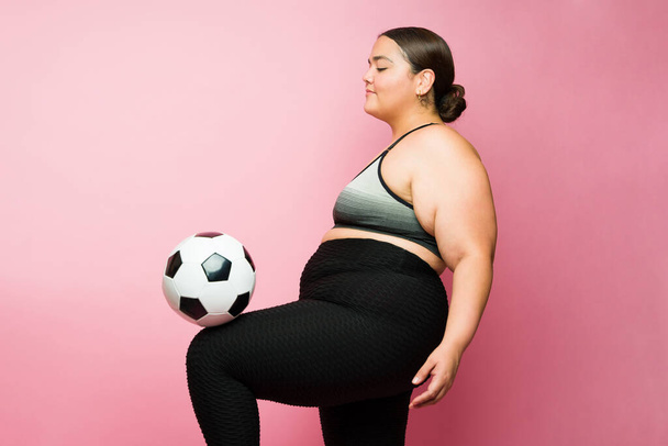Active fat latin woman in activewear playing with a soccer ball while exercising and training sports  - Foto, Bild
