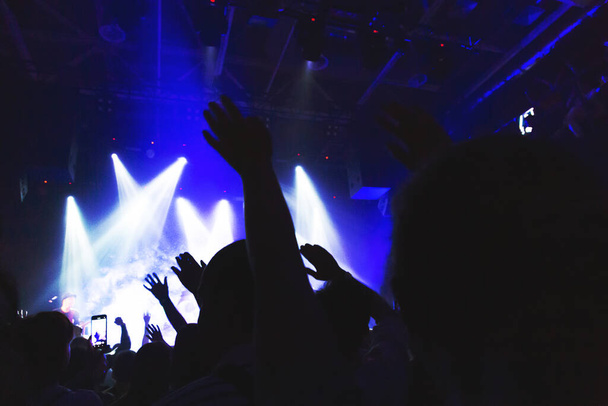 Силуэты концертной толпы перед освещенной сценой в ночном клубе. Дым, прожекторы концертов
. - Фото, изображение