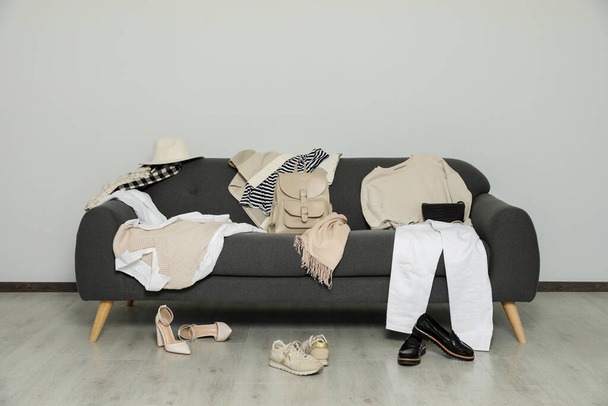 Messy pile of clothes on sofa and shoes in living room - Фото, изображение