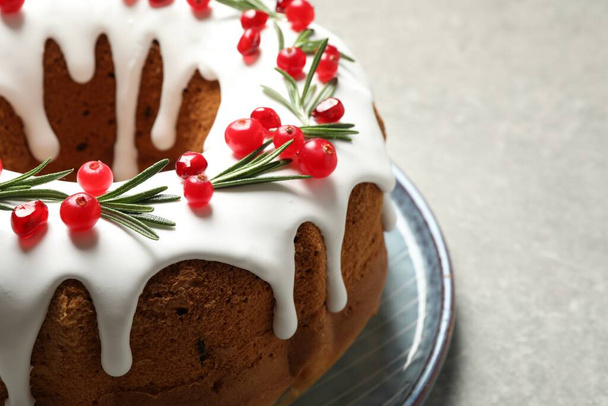 Traditional Christmas cake decorated with glaze, pomegranate seeds, cranberries and rosemary on light grey table, closeup - Zdjęcie, obraz