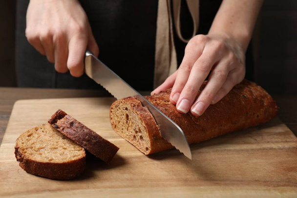 Woman cutting freshly baked rye baguette at wooden table, closeup - Fotó, kép