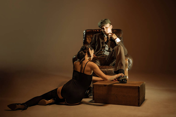 Feelings. Vintage style portrait of man and woman in 1920s style fashion outfits isolated over dark brown background. Concept of business, personality, emotions, family, art, fashion - Φωτογραφία, εικόνα