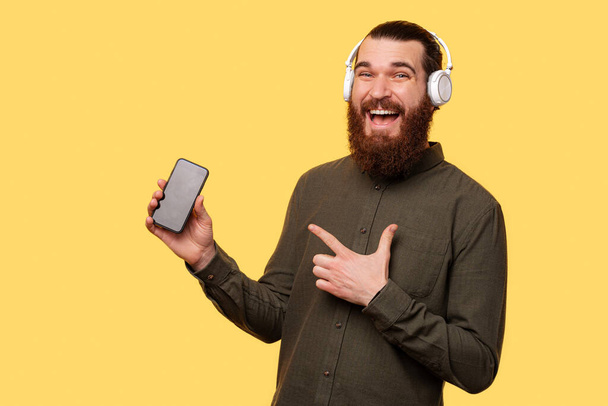 A picture of a man with headphones pointing to his new phone - Fotoğraf, Görsel