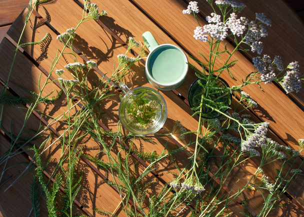 Yarrow plants and glass of yarrow herb tea on wooden table, top view. Traditional medicine. - Fotó, kép