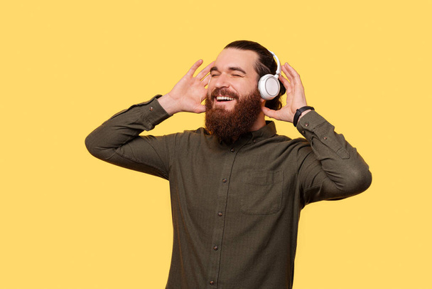 A bearded man is joyfuly enjoying the music he listens through his new headphones - Photo, image