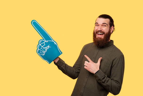 A photo of a man holding his fan glove and smiling is pointing at a free space - Photo, Image