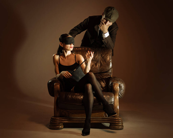 Intrigue. Vintage style portrait of man and woman in 1920s style fashion outfits isolated over dark brown background. Concept of business, personality, emotions, family, art, fashion - 写真・画像