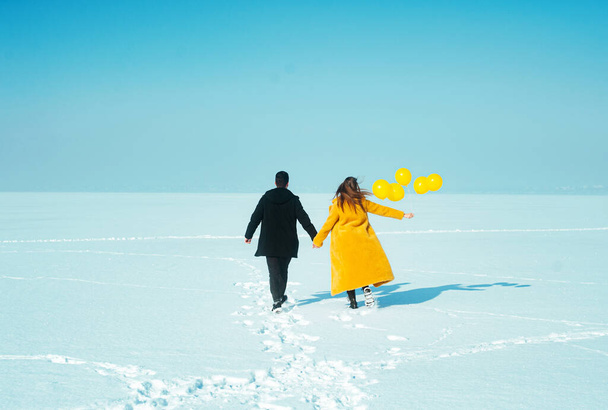 young couple with yellow balloons has fun outdoors,happy walking couple. In love man and woman walking on the snowy ice - Foto, Bild