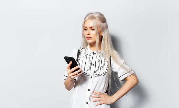 Studio portrait of young blonde pretty girl looking in smartphone on white background. - Fotografie, Obrázek