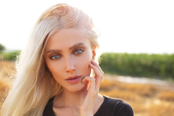 Крупним планом портрет красивої молодої блондинки з блакитними очима на тлі сонячного світла. Натуральне фото на відкритому повітрі
. - Фото, зображення