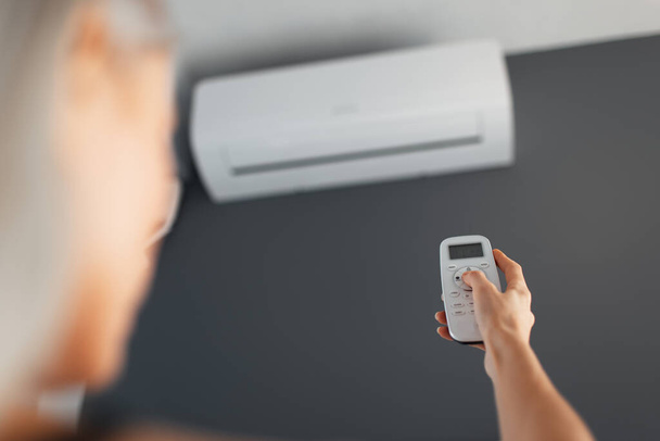 Young blonde female holds remote control of the air conditioner. - Foto, imagen