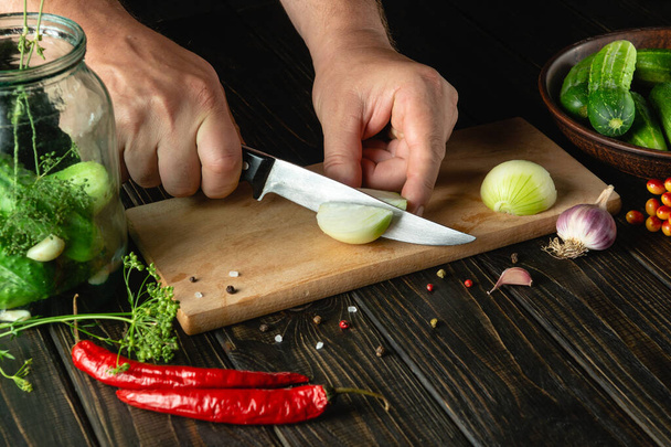 Slicing onions on a cutting board by the hands of a cook for pickling or salt in a jar with cucumbers and spices. Menu for restaurant or hotel. - Fotó, kép