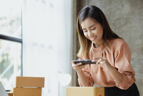 A woman using a smartphone to take pictures in front of parcel boxes, parcel boxes for packing goods, delivering goods through private courier companies. Online selling and online shopping concepts. - Foto, immagini