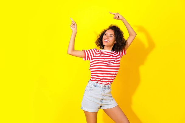 Portrait of young smiling happy woman directing empty space new brand shopping isolated on yellow color background. - Photo, Image