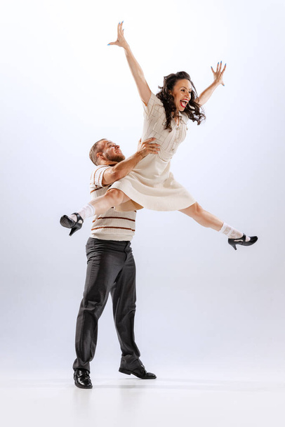 Rhythm and expression. Energetic dance couple in retro style outfits dancing lindy hop, jive isolated on white background. Timeless traditions, 60s ,70s american fashion style. Emotions, expressions - Фото, изображение