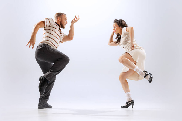 Rhythm and expression. Energetic dance couple in retro style outfits dancing lindy hop, jive isolated on white background. Timeless traditions, 60s ,70s american fashion style. Emotions, expressions - Фото, зображення