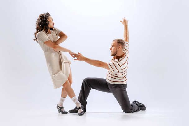 Music and dance. Astonished young man and woman in retro style outfits dancing lindy hop isolated on white background. Timeless traditions, 60s ,70s american fashion style. Emotions, expressions - Fotó, kép