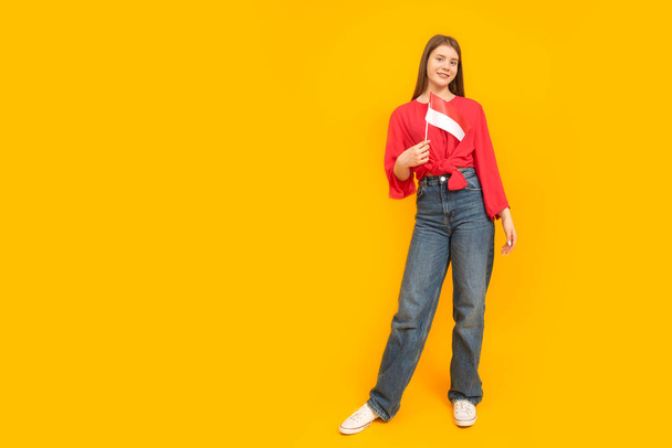 Full-length portrait of young girl on yellow background. Teenager holds the flag of Monaco or Indonesia - Foto, Bild