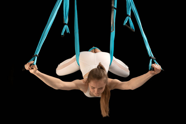 Woman practicing fly yoga using hammock suspended from the ceiling. Girl gymnast in trapeze class. Black background - Foto, Imagem