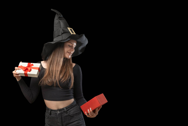 Happy young woman in pointed witches hat with opened gift in hands. Copy space. Isolation on black background. Halloween - 写真・画像