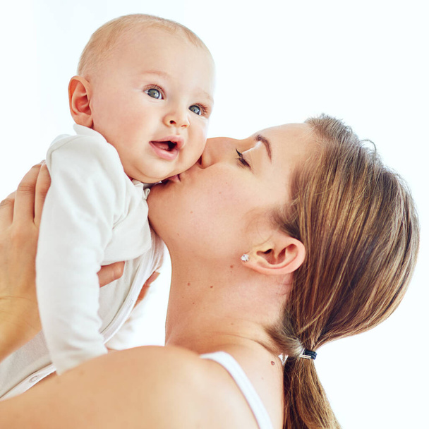 Loving, caring and affectionate mother kissing and bonding with her baby. Female embracing motherhood holding her baby in the air enjoying a sweet moment of love, care and happiness. - Photo, Image