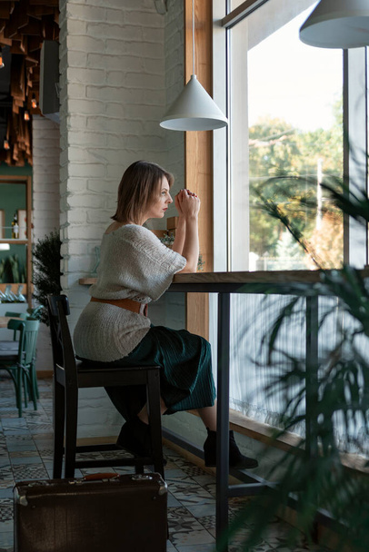 Portrait of mature woman in cafe. Middle aged woman sits at table in cozy cafe near large window. Vertical frame - Φωτογραφία, εικόνα