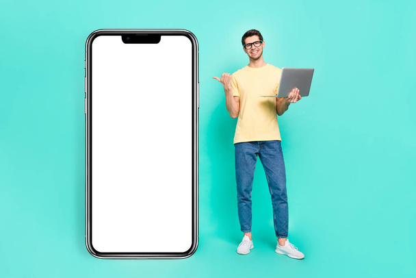 Full length photo of ceo brunet young guy hold laptop index promo wear eyewear t-shirt jeans shoes isolated on teal background. - Φωτογραφία, εικόνα