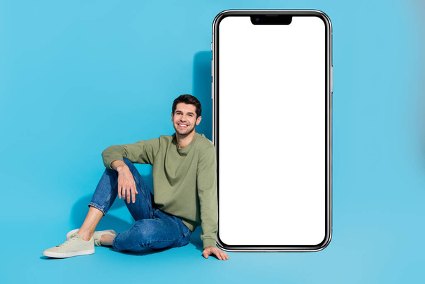 Full body portrait of positive person sit floor empty space huge phone isolated on blue color background. - Valokuva, kuva
