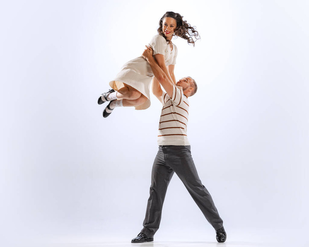 Jumping. Astonished young dancing man and woman dance sport dances isolated on white background. Timeless traditions, 60s ,70s american fashion style. - Photo, Image