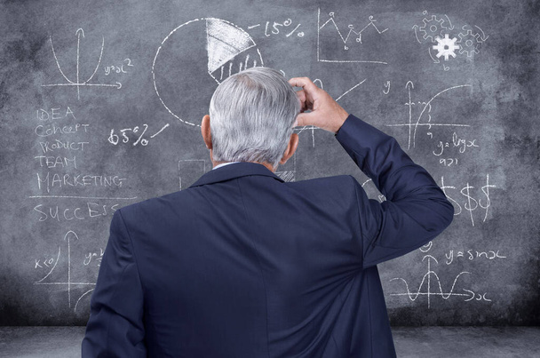 Professional finance corporate business man thinking of investment, figuring out a problem and dealing with stock market crash on a black chalkboard. Manager looking confused while making a decision. - Photo, image