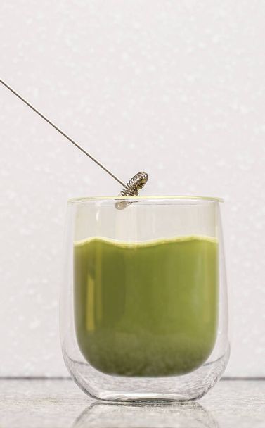 Green matcha latte tea in a glass. Green matcha latte is poured into a transparent glass with a double bottom - Zdjęcie, obraz
