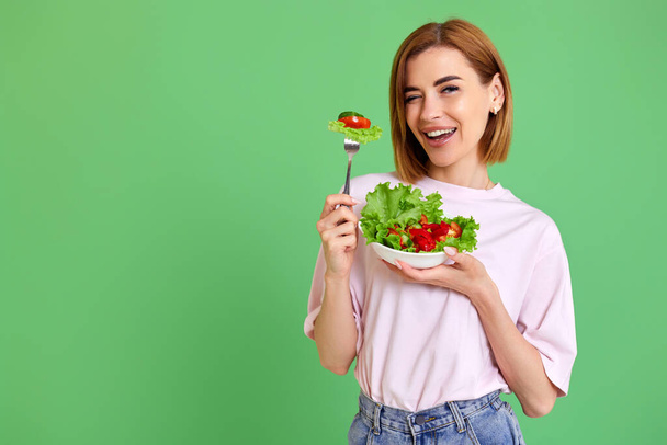 beautiful smiling healthy woman eating fresh vegetable salad, looking happy on green background - Foto, Imagem