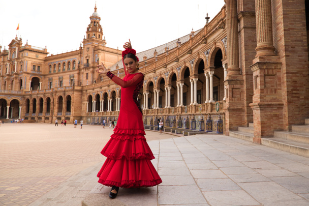 Beautiful teenage woman dancing flamenco in a square in Seville, Spain. She wears a red dress with ruffles and dances flamenco with a lot of art. Flamenco cultural heritage of humanity. - Zdjęcie, obraz