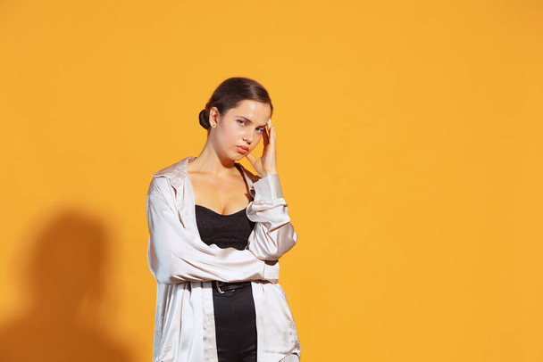 Portrait of young beautiful woman posing with thoughtful, tired expression posing isolated over yellow studio background. Concept of beauty, lifestyle, youth, emotions, facial expression, ad - Photo, image