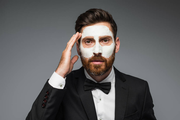 bearded man in suit with clay mask on face adjusting hair isolated on grey  - Fotó, kép