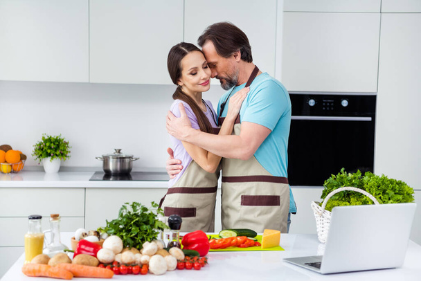 Photo of charming pretty age boyfriend girlfriend wear aprons cook breakfast embracing indoors room home. - Foto, imagen