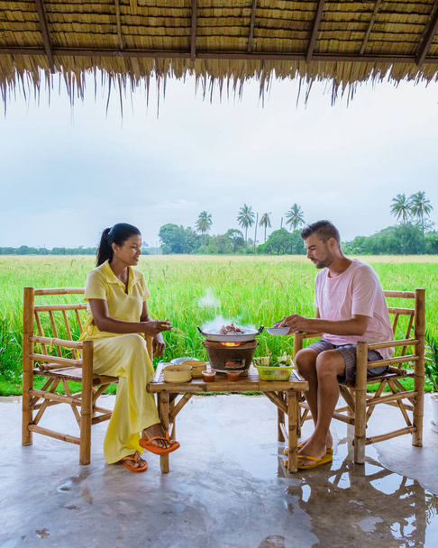 couple men and women having a Korean bbq on vacation at a homestay in Thailand, eco farm with green rice paddy field during monsoon season in Thailand - Photo, Image